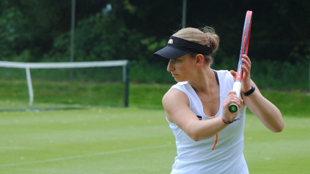 Tennis player dressed in white on a grass court with tennis visor